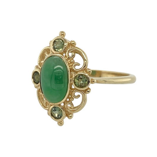 This pre-owned 9ct yellow gold jade and green stone ring is a distinctive design, combining a central oval jade with four complementary green stones.

Design: Featuring an oval jade stone at the centre, this ring is accented by four round green stones arranged around it for added colour and detail. The warm yellow gold setting complements the different green tones, creating an eye-catching piece with a classic gemstone look.
Material: Made from 9-carat yellow gold.