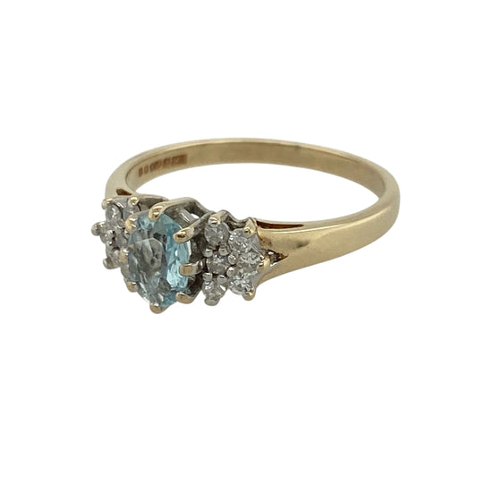 This pre-owned 9ct yellow gold diamond and blue topaz ring is a colourful design, featuring a central oval blue topaz accented by small diamond clusters.

Design: Featuring an oval blue topaz at the centre with a small diamond cluster set on either side, this ring combines the bright blue tones of topaz with classic yellow gold and delicate diamond detail.
Material: Made from 9-carat yellow gold.