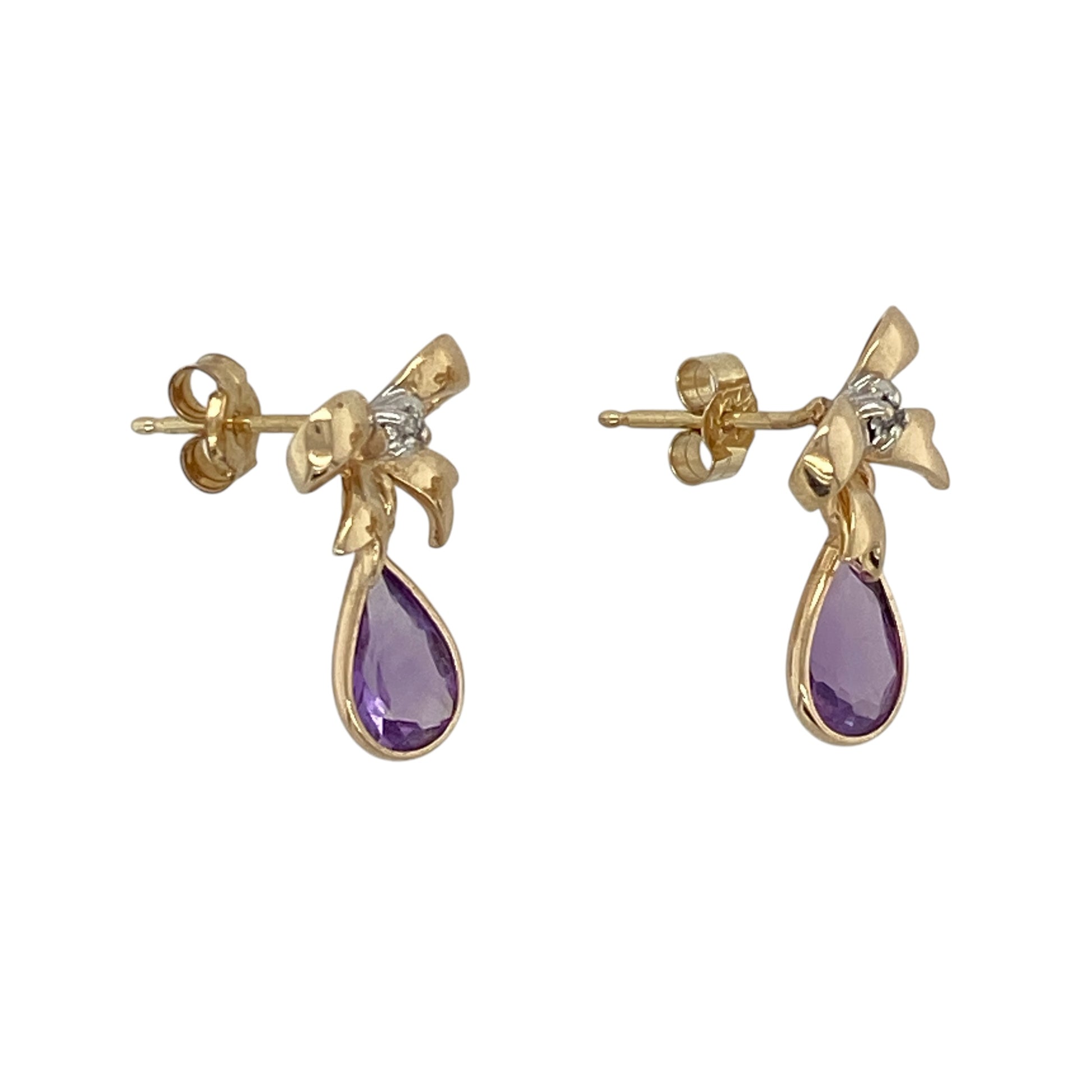 These pre-owned 9ct yellow gold diamond and amethyst bow drop earrings are a decorative design, featuring teardrop amethyst stones with diamond detailing.

Design: Featuring a bow-style design with teardrop amethyst drops and diamond detailing, these earrings combine a decorative shape with the warm finish of 9ct yellow gold.
Material: Made from 9-carat yellow gold.
Gemstone Detail: Teardrop amethyst stones each measuring approximately 7mm by 5mm with diamond detailing.