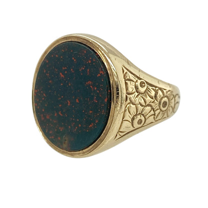 This pre-owned 9ct yellow gold and bloodstone oval signet ring is a substantial traditional design, featuring a large oval bloodstone with decorative flower-patterned shoulders.

Design: Featuring an oval bloodstone centre with flower-patterned detailing along the shoulders, this signet ring has a bold traditional design finished in warm 9ct yellow gold.
Material: Made from 9-carat yellow gold.
Gemstone Detail: Oval bloodstone measuring approximately 17mm by 14mm.
