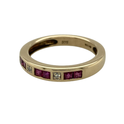 This pre-owned 9ct yellow gold diamond and ruby band ring is a classic gemstone design, featuring square rubies with diamond detailing.

Design: Featuring six square ruby stones with two diamonds set across the front, this band ring combines rich red tones with the warm finish of 9ct yellow gold.
Material: Made from 9-carat yellow gold.
Gemstone Detail: Set with six square rubies and two diamonds.
Ring Detail: Front of the band measures approximately 3mm wide.