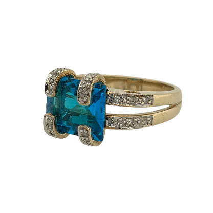 This pre-owned 9ct yellow gold diamond and blue stone ring is a striking dress ring, featuring a large blue centre stone with diamond-set detailing.

Design: Featuring a large blue centre stone, this ring has decorative diamond-set gold claws and diamond-set shoulders finished in warm 9ct yellow gold.
Material: Made from 9-carat yellow gold.
Gemstone Detail: Set with a blue stone measuring approximately 11mm by 9mm, complemented by diamonds set into the gold claws and shoulders.