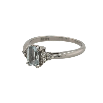 This pre-owned 9ct white gold diamond and aquamarine-coloured stone ring is a classic gemstone design, featuring a rectangular centre stone complemented by diamond detailing.

Design: Featuring a rectangular aquamarine-coloured centre stone, this ring has three diamonds set on either side for a balanced design in 9ct white gold.
Material: Made from 9-carat white gold.
Gemstone Detail: Set with a rectangular aquamarine-coloured stone measuring approximately 6mm by 4mm, with three diamonds set on either side.