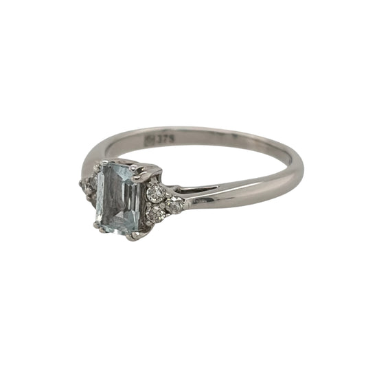 This pre-owned 9ct white gold diamond and aquamarine-coloured stone ring is a classic gemstone design, featuring a rectangular centre stone complemented by diamond detailing.

Design: Featuring a rectangular aquamarine-coloured centre stone, this ring has three diamonds set on either side for a balanced design in 9ct white gold.
Material: Made from 9-carat white gold.
Gemstone Detail: Set with a rectangular aquamarine-coloured stone measuring approximately 6mm by 4mm, with three diamonds set on either side.