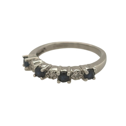 This pre-owned 9ct white gold diamond and sapphire band ring is a classic gemstone design, featuring four round sapphires complemented by diamond detailing.

Design: Featuring a traditional gemstone band design, this ring has four round sapphires arranged across the front with diamond detailing in 9ct white gold.
Material: Made from 9-carat white gold.
Gemstone Detail: Set with four round sapphires measuring approximately 3mm in diameter each, complemented by diamond detailing.