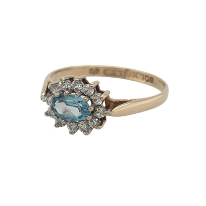This pre-owned 9ct yellow gold blue topaz and cubic zirconia cluster ring is a classic gemstone design, featuring an oval blue topaz surrounded by contrasting cubic zirconia stones.

Design: Featuring a traditional cluster design, this ring showcases an oval blue topaz centre stone surrounded by cubic zirconia detailing in warm 9ct yellow gold.
Material: Made from 9-carat yellow gold.
Gemstone Detail: Set with an oval blue topaz measuring approximately 6mm by 4mm, surrounded by cubic zirconia stones.
