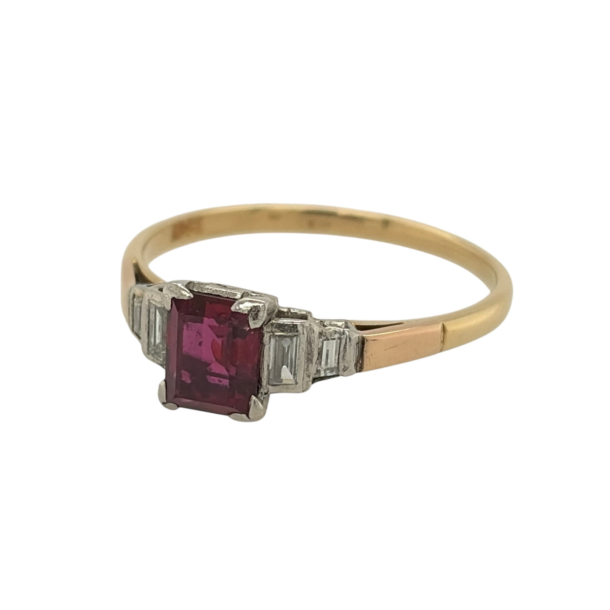 This pre-owned 18ct yellow gold diamond and ruby vintage-style ring is a distinctive gemstone design, featuring an emerald cut ruby with baguette cut diamond detailing.

Design: Featuring a vintage-style setting, this ring showcases a central emerald cut ruby with two baguette cut diamonds set on either side in warm 18ct yellow gold.
Material: Made from 18-carat yellow gold.