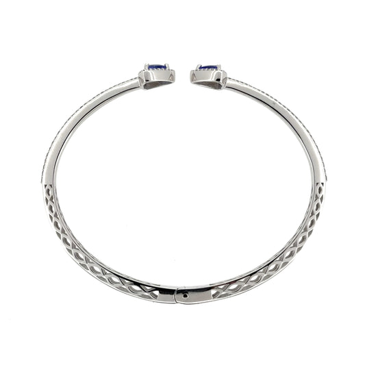 This pre-owned 18ct white gold diamond and tanzanite bangle is a striking torque-style design, featuring tanzanite stones with detailed diamond setting.
Design: Featuring an open torque-style design, this bangle has a triangular tanzanite stone at each end, surrounded by diamonds, with a double row of diamonds extending around half of the bangle.
Material: Made from 18-carat white gold.