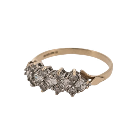 Add classic stone-set detail to your jewellery collection with this pre-owned 9ct yellow gold cubic zirconia cluster band ring, featuring a combination of round and square-cut stones.

Design: The ring features a cluster-style band design, combining round and square-cut cubic zirconia stones across the front for a detailed and distinctive appearance.
Material: Made from 9-carat yellow gold, the warm gold tone provides a classic setting for the cubic zirconia stones.