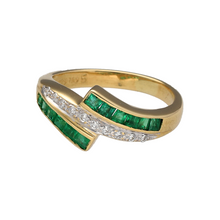 Load image into Gallery viewer, Add a touch of vibrant luxury to your jewellery collection with this pre-owned 18ct yellow gold diamond and emerald crossover band ring—an elegant blend of colour, sparkle, and timeless design.

Design: The ring features a striking crossover layout with brilliant diamonds set in the centre, framed by square-cut emeralds along the top and bottom. The band measures 9mm wide at its widest point, creating a bold and balanced silhouette.

