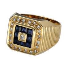 Load image into Gallery viewer, Bring bold sophistication and vintage luxury to your collection with this pre-owned 18ct yellow gold diamond and sapphire set halo signet ring—a standout design with rich detail, strong structure, and radiant sparkle.

Design: The ring features a striking 15mm high front with a central diamond framed by a halo of square-cut sapphires, encircled by an outer row of brilliant-cut diamonds. The wide shoulders are textured, adding depth and character to the overall design.


