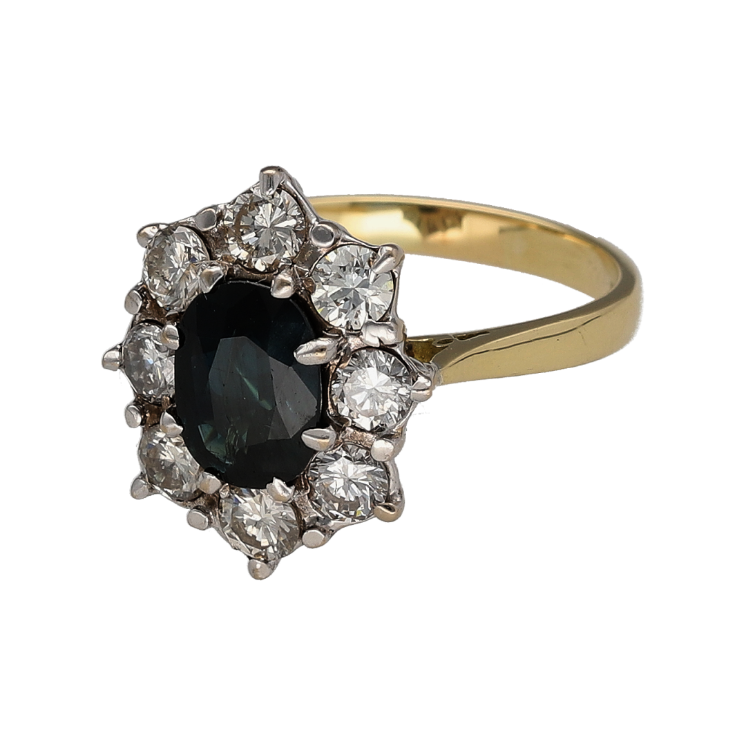 Add exceptional sparkle and timeless elegance to your jewellery collection with this pre-owned 18ct yellow gold diamond and sapphire cluster ring, featuring a stunning gemstone design with luxurious statement appeal—perfect for special occasions, gifting, or sophisticated everyday wear.

Design: The ring showcases a beautiful oval sapphire measuring approximately 8mm by 6mm, creating a striking focal point with its rich blue colour.